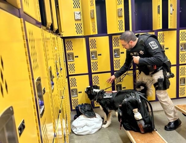 A jail deputy and narcotics detecting dog search for drugs in the locker room of a local school.